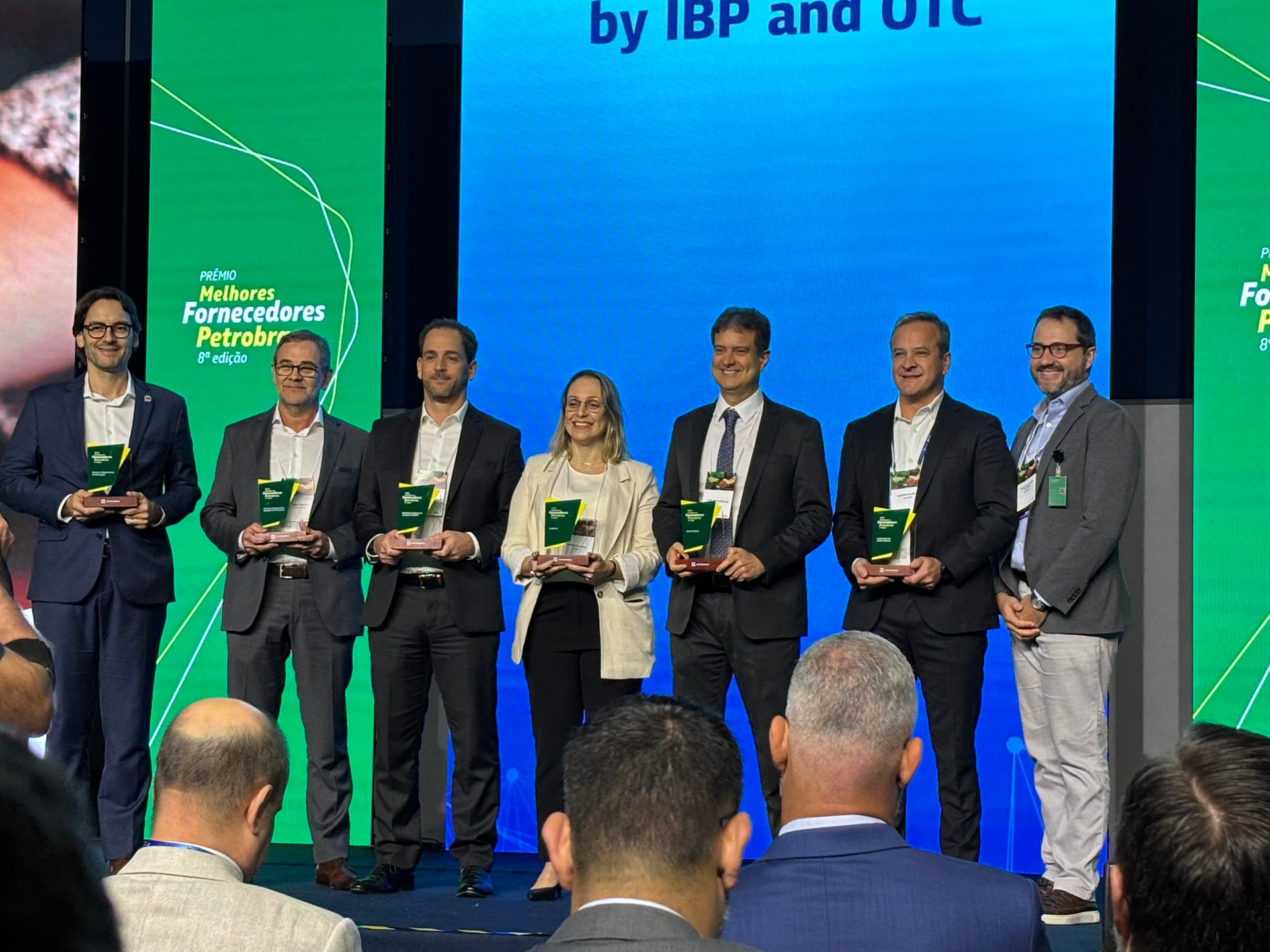 NOV's APL group standing on stage holding awards during the Petrobras’ Best Suppliers Awards, with a presentation screen and audience visible in the forefront.