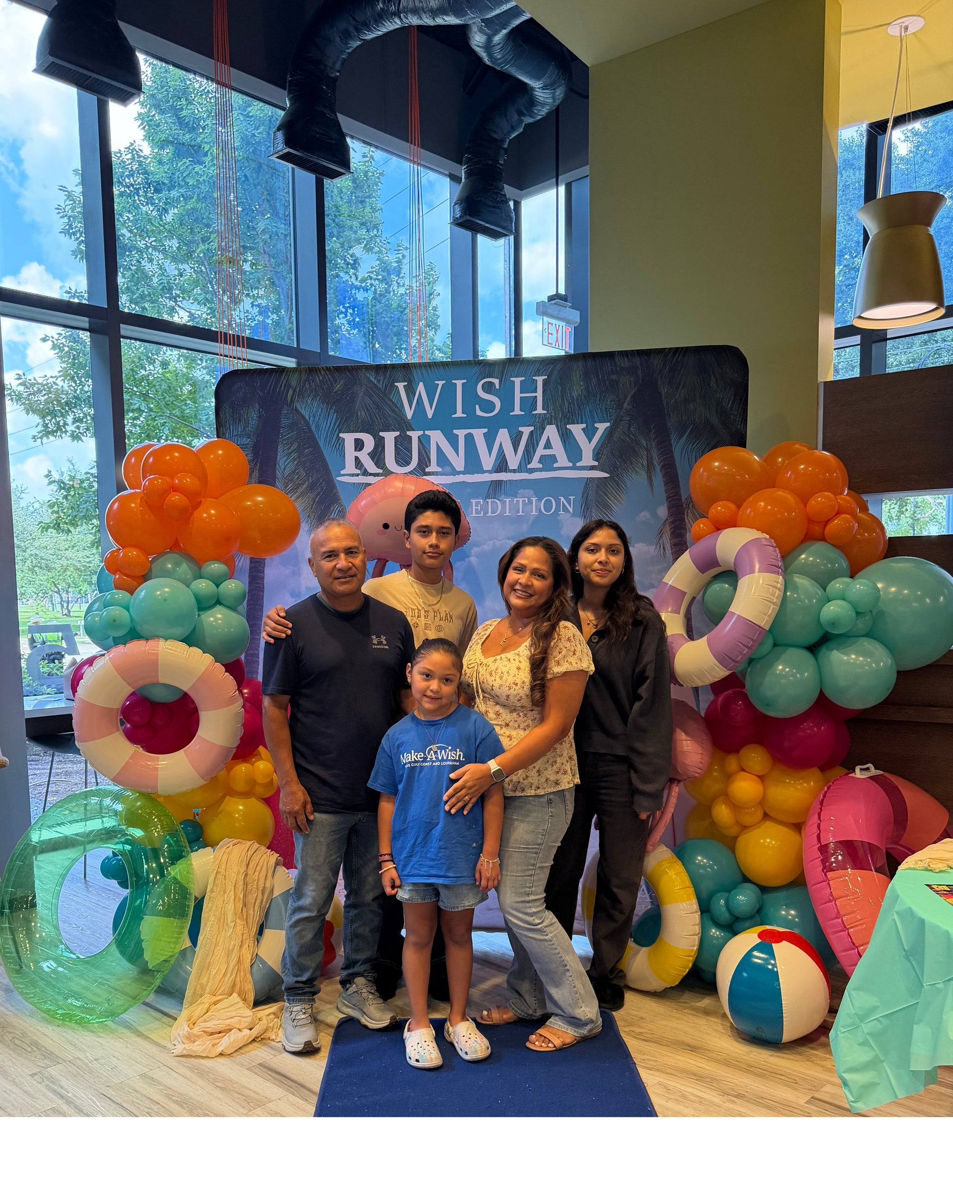 Mia and her family standing in front of a large banner while at a Make-a-Wish event at the NOV office