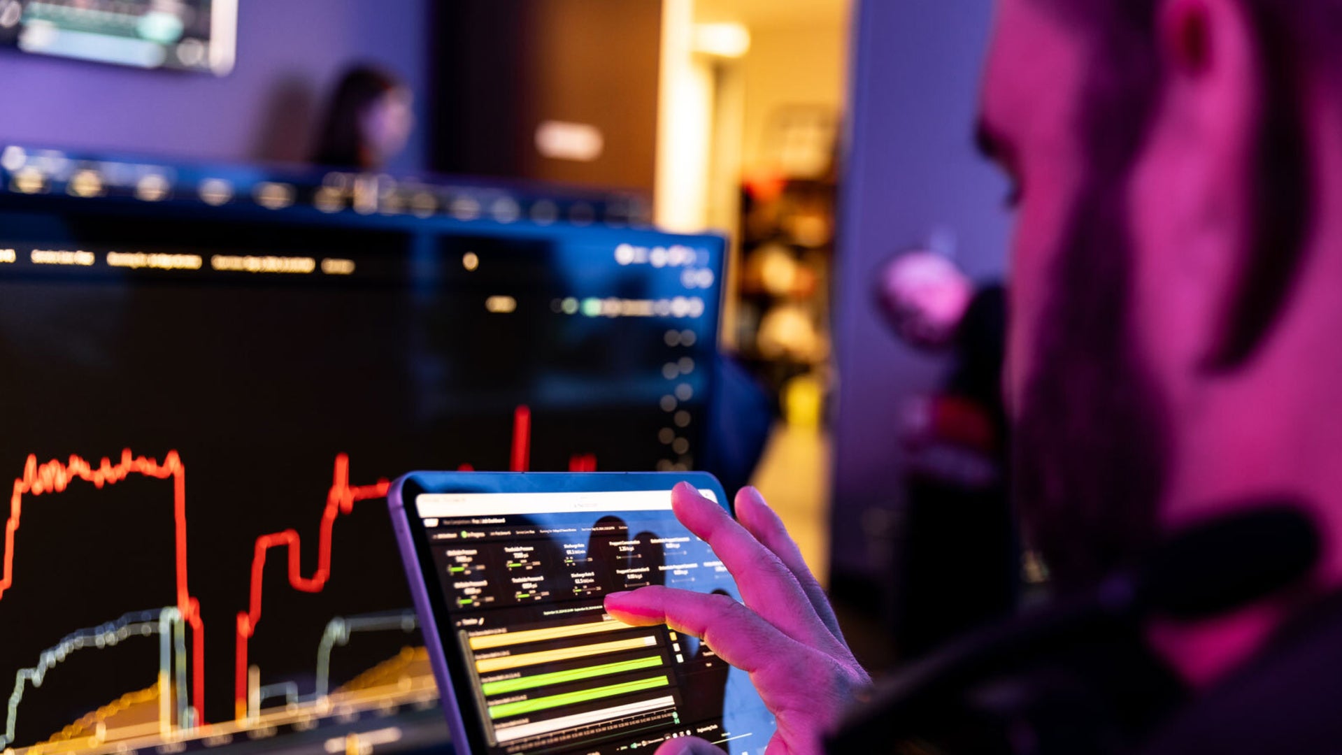 Person reviewing data on a touch screen device with more screens showing data on the wall