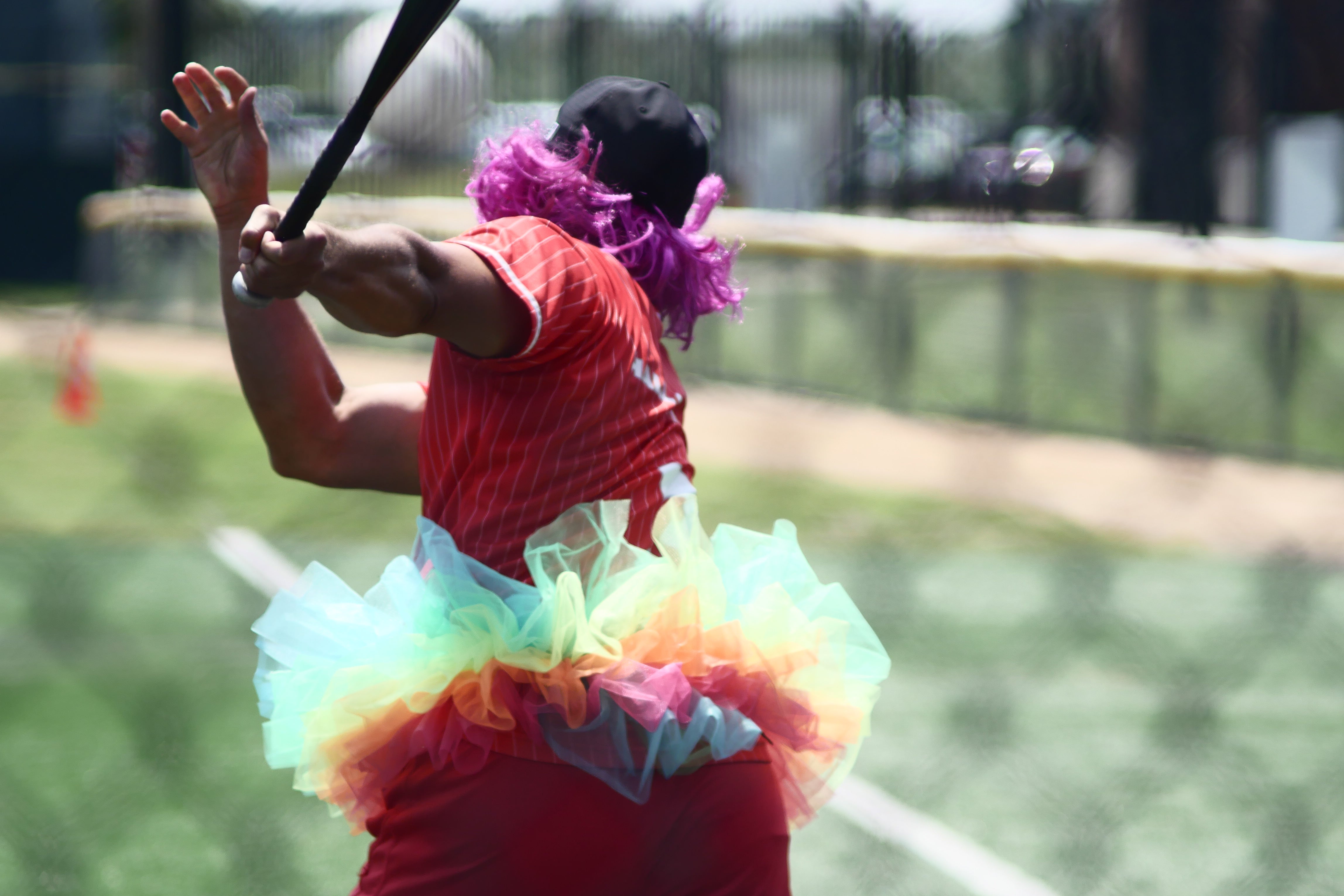 Softball player running after swinging while wearing a purple wig with a cap, and a colorful tutu at the Derricks and Diamonds charity tournament