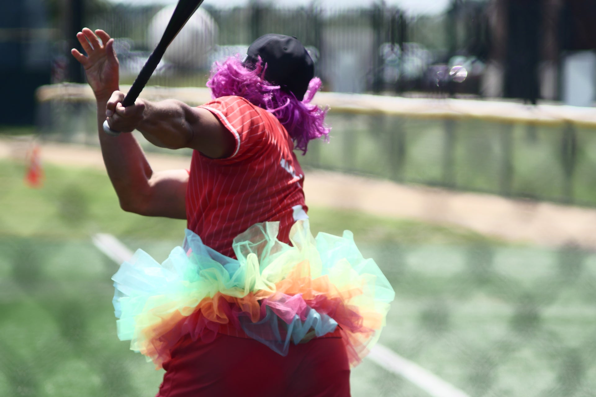 Softball player running after swinging while wearing a purple wig with a cap, and a colorful tutu at the Derricks and Diamonds charity tournament