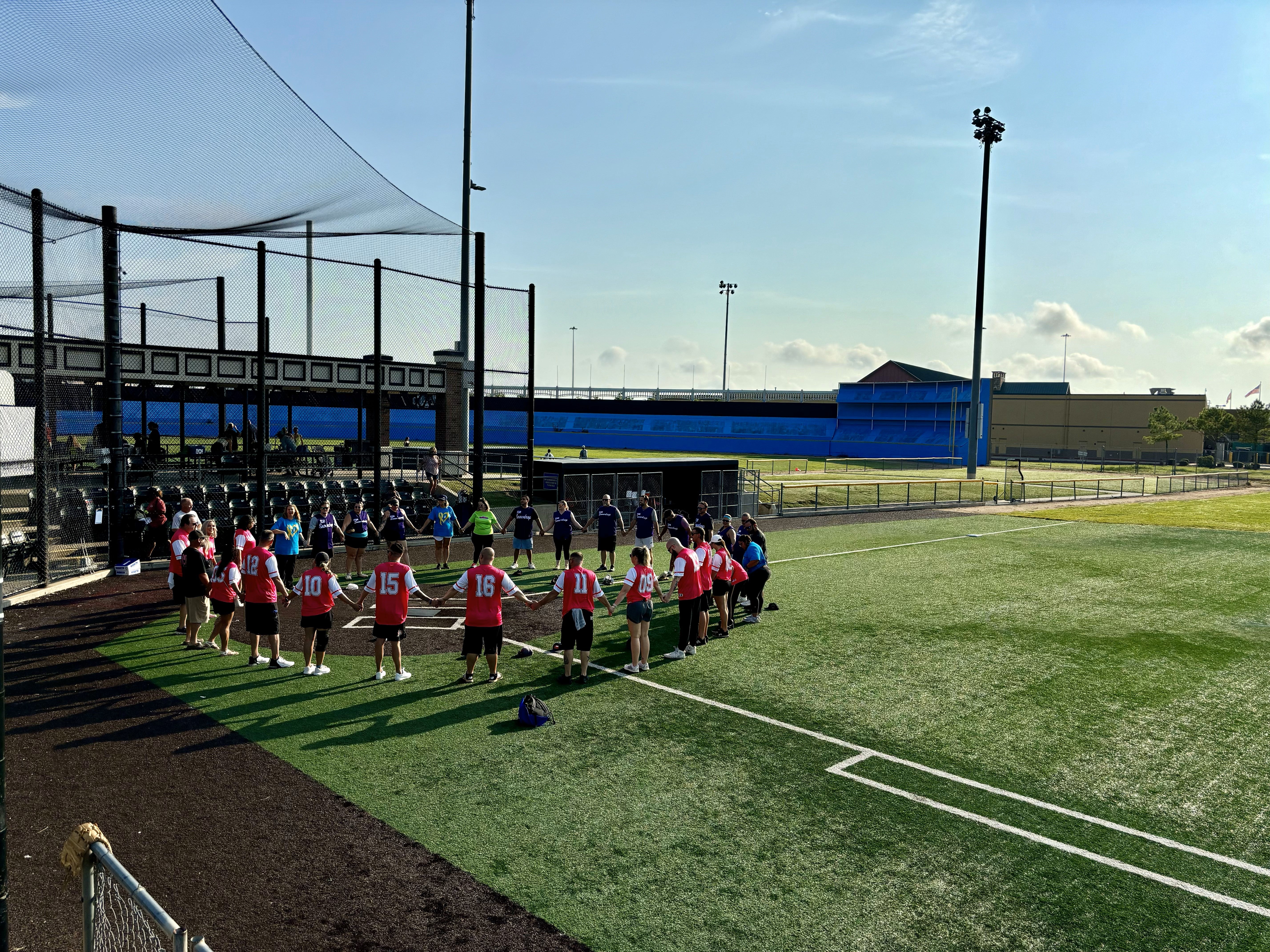 Group of people in a circle holding hands while on a softball field
