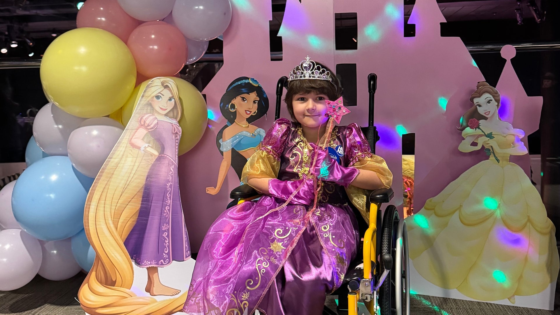 Young child in a wheelchair dressed as a princess with a colorful backdrop display