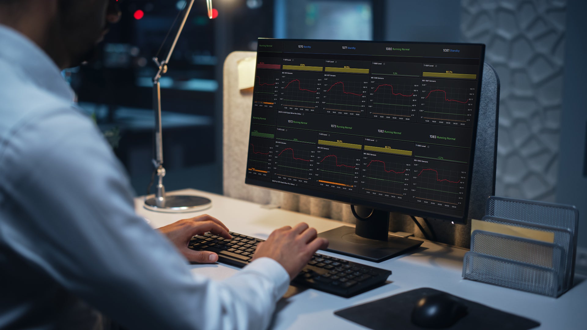 Person working at a desk with a computer monitor displaying Intelligent Equipment Monitoring data in a dark office setting