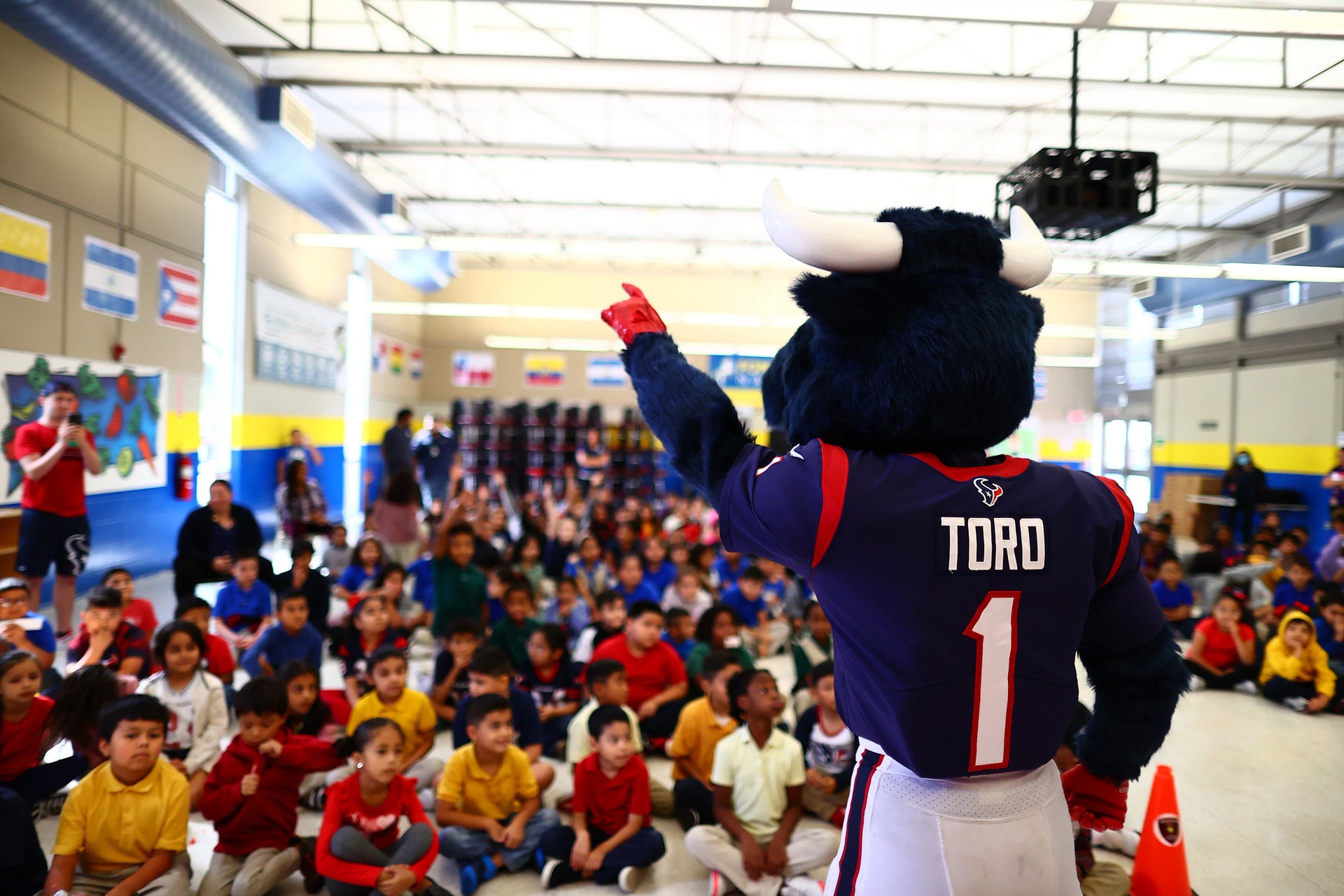 Group of students sitting on the floor watching the Texans mascot TORO in a school cafeteria